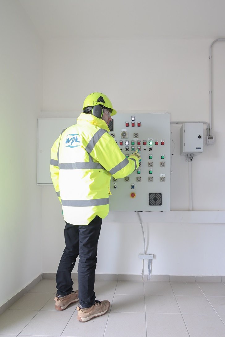 WPL employee looking at the control panel housed in the gabion stone wall entrance to the site at Drinov.